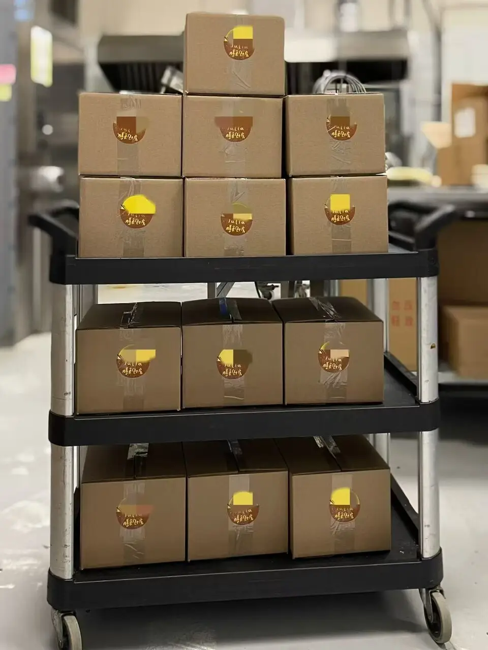 More than a dozen kraft-paper meal boxes stacked on a kitchen cart, each sealed with a round Julia's Kitchen sticker