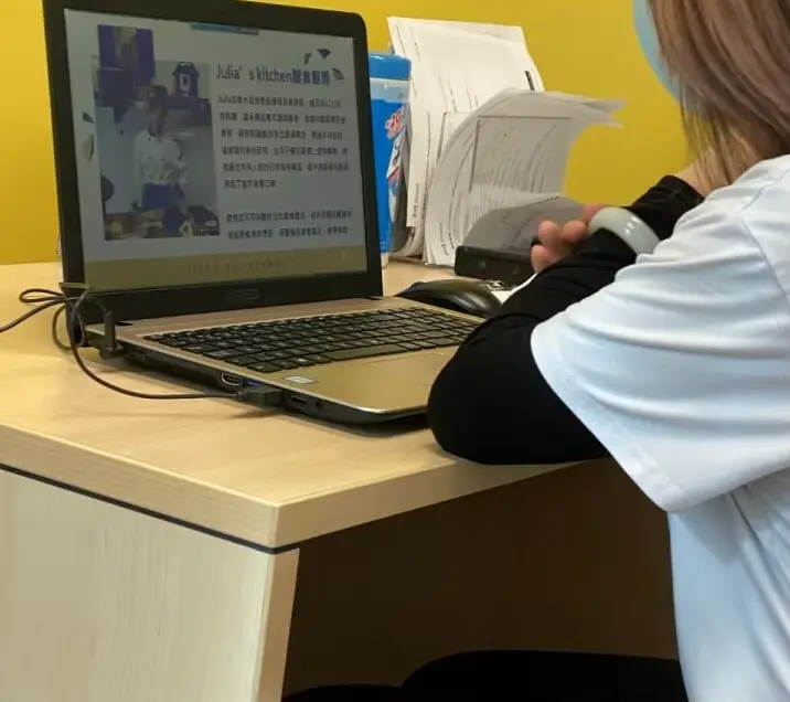 A laptop on a desk showing the Chinese introduction page for Julia's Kitchen, with a photo of a cook in chef's whites, beside someone sorting paperwork