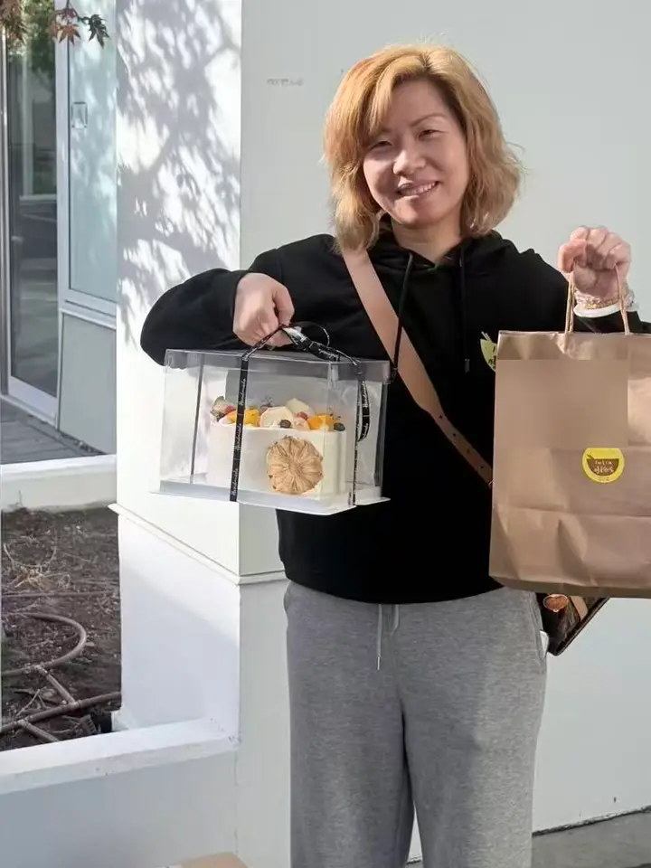 Julia outside a client's door holding a fresh-fruit cake in one hand and, in the other, a kraft-paper bag with a round Julia's Kitchen sticker containing a gift pack of baby-cleaning essentials