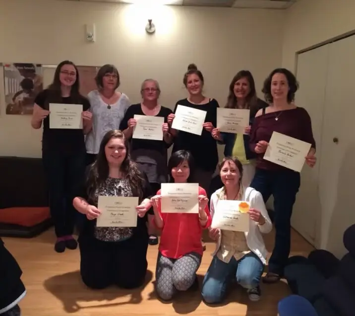 Julia, in a red top in the front row, in a group photo with the others who completed the course, each holding a certificate of completion