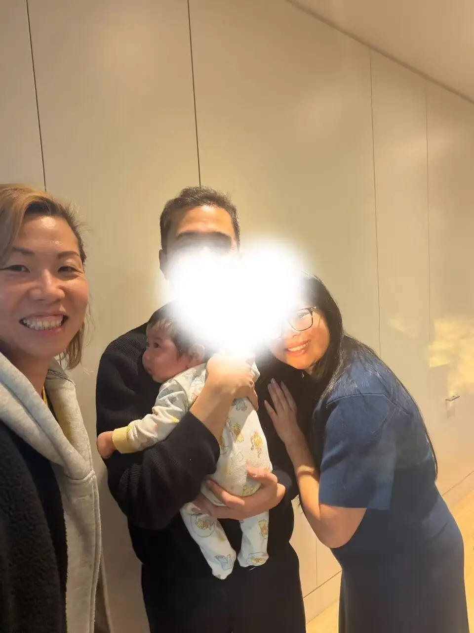 Julia with a returning client family, the father holding their two-month-old baby and the mother leaning in beside him, smiling