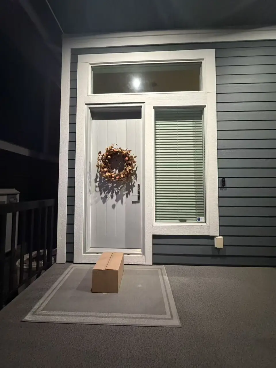 A confinement meal delivery box left at a client's front door after dark, on the doormat under the porch light